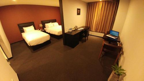 a hotel room with two beds and a desk with a laptop at Gangneung Tourist Hotel in Gangneung