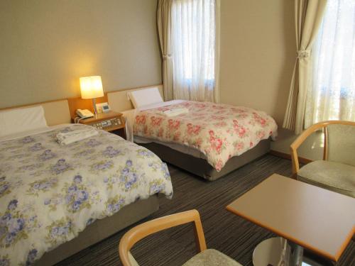 a hotel room with two beds and a table and chairs at Center Hotel Mihara in Mihara