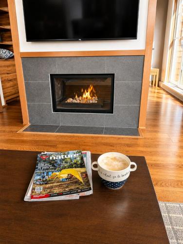 a coffee table with a book and a cup of coffee and a fireplace at Appartement-Condo sur Lac Superieur-Mont-Tremblant in Lac-Superieur