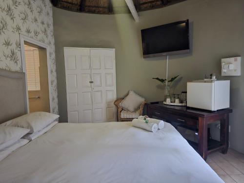 a bedroom with a white bed with a tv on the wall at Woodpecker cottage in Hartbeespoort
