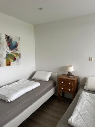 a bedroom with two beds and a nightstand with a painting at Bungalow kleine Deichperle, Strand, Deich und ein wunderschöner kleiner Ort in unmittelbarer, fußläufger Nähe! in Lemmer