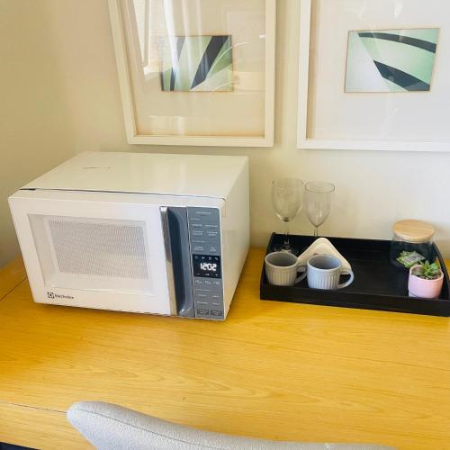 a microwave sitting on a wooden table with glasses at Flat de Luxo Aeroporto Congonhas - Hotel in São Paulo
