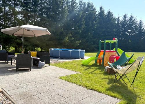 a patio with chairs and an umbrella and a playground at Mazury w Zasięgu in Brajniki