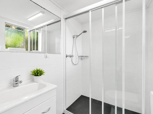 a white bathroom with a shower and a sink at Tradewinds Apartments in Coffs Harbour
