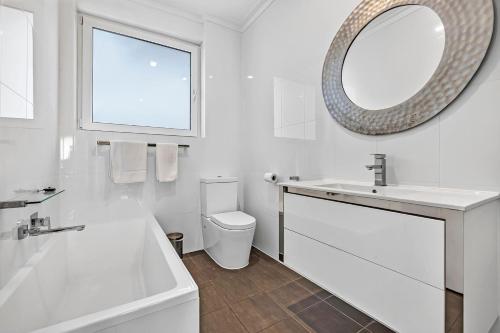 a white bathroom with a tub and a sink and a mirror at Sunset Sands on Esplanade By Host Solutions in West Beach