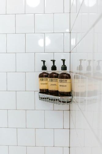 four bottles of soap on a shelf in a white tiled bathroom at Cache House in Jackson