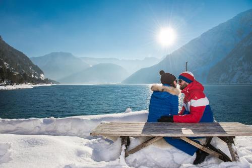 a man and a woman sitting on a bench in the snow at Alpenherz Ferienwohnungen in Pertisau