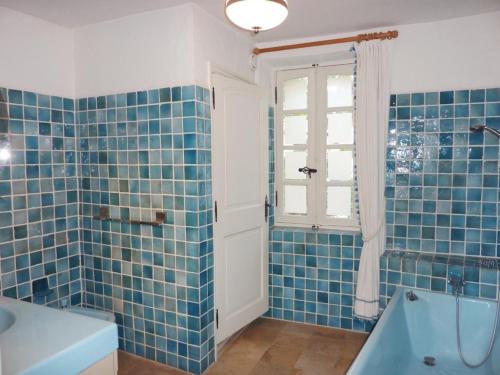 - une salle de bains carrelée de bleu pourvue d'une baignoire et d'une fenêtre dans l'établissement Maison au cœur du Village, à Gassin