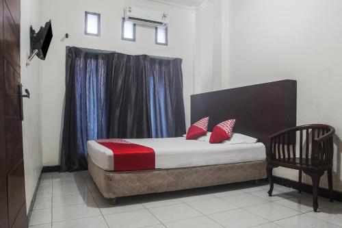 a bed with red pillows and a chair in a room at Hotel O Icha Homestay in Makassar
