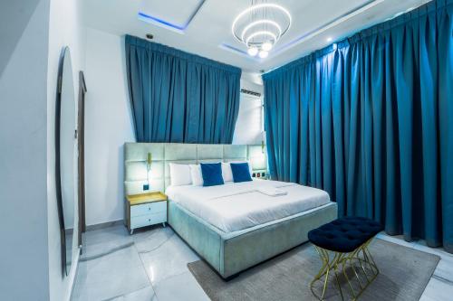 a bedroom with blue curtains and a bed and a stool at One90 Apartment in Lagos