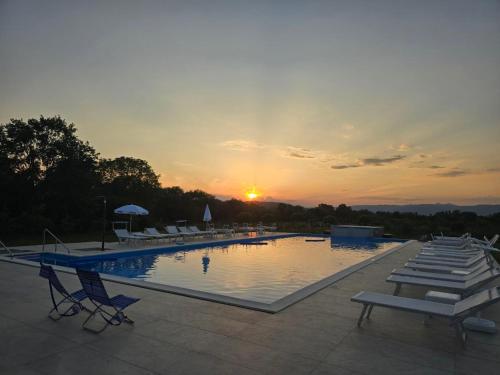 a swimming pool with chairs and a sunset in the background at Pensiunea Cocosel in Căstău