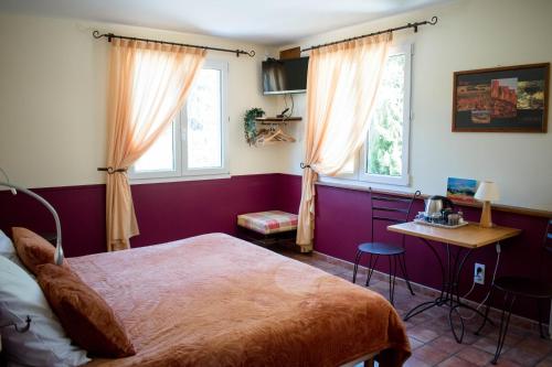 a bedroom with a bed and a table and two windows at Chambres à la Table du Curé in Cucugnan
