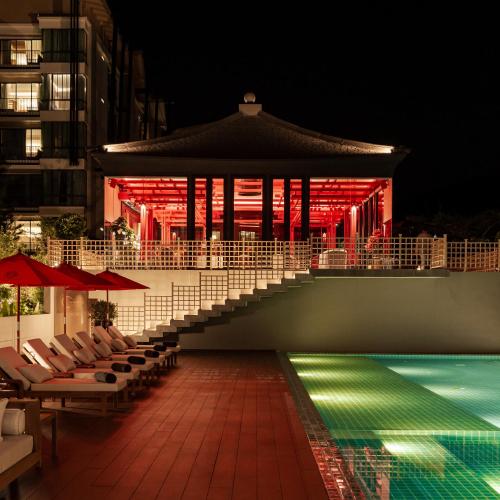a pool with chairs and a building with red lights at Zen Essence Khao Yai in Khao Yai