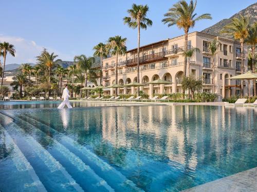 a person walking by a swimming pool in front of a building at Grecotel Filoxenia Kalamata in Kalamata