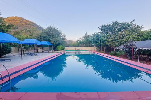 a swimming pool with blue water and blue umbrellas at Sariska Forest Trail in Rāmsinghpura