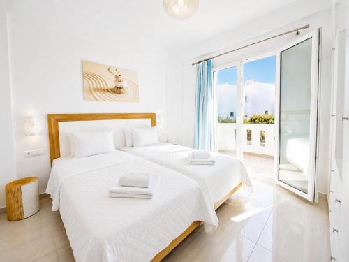 a white bedroom with two beds and a large window at Eleftheria Hotel & Apartments in Ornos