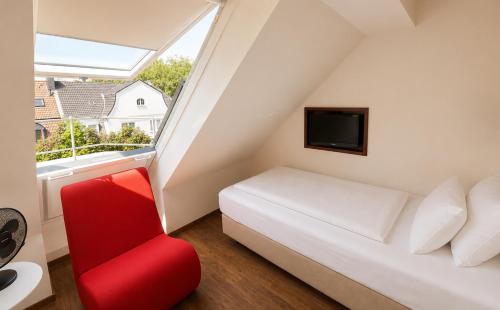 a bedroom with a bed and a red chair at DORMERO Hotel Essen in Essen