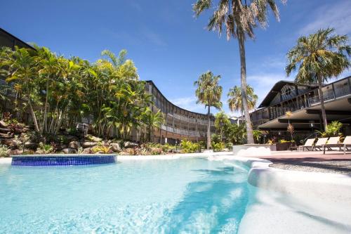 a swimming pool in front of a building with palm trees at Mantra Club Croc in Airlie Beach
