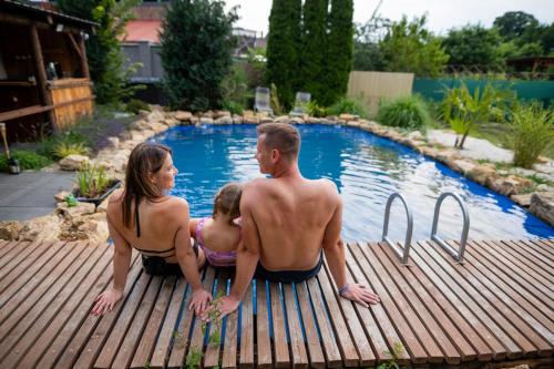 a group of three people sitting on a wooden deck near a swimming pool at Wellness Glamping Apartmán Přerov in Přerov