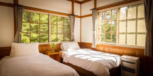 two beds in a room with two windows at Kamishiro Mountain Lodge in Hakuba