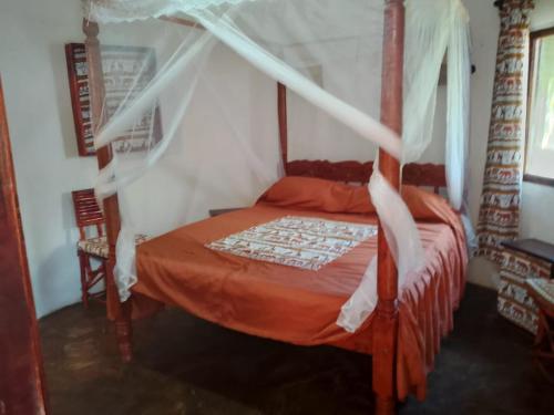 a bedroom with a canopy bed with an orange comforter at Al Mar Bed and Breakfast in Watamu