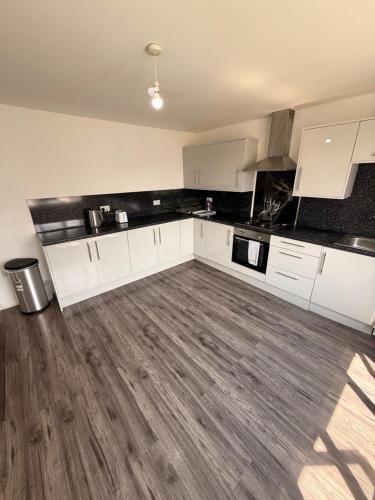 an empty kitchen with white cabinets and a wooden floor at 3 Bedroom Central Apartment in Goodmayes