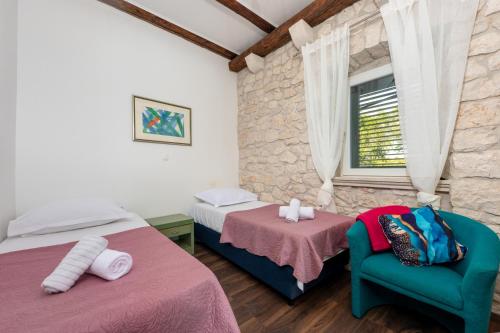 a bedroom with two beds and a chair and a window at Authentic Dalmatian Stone House-Kameni dvori in Selca kod Bogomolja