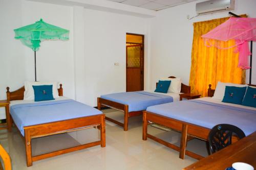 a room with three beds with blue sheets and a pink umbrella at Trinco Eddi Resort in Trincomalee