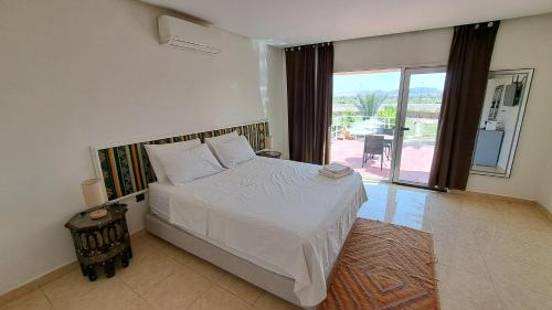 a bedroom with a white bed and a large window at Les Plamiers d'anis in Ouarzazate