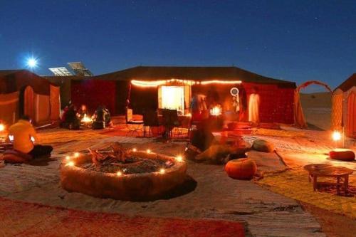 a group of people sitting outside of a tent at night at Sahara Starlight camp in Merzouga