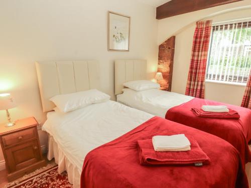 two beds in a room with red sheets at The Coach House in Wigton