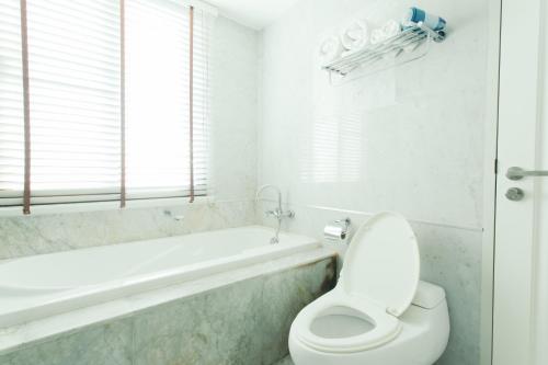 a white bathroom with a toilet and a bath tub at Thomson Residence Hotel in Bangkok