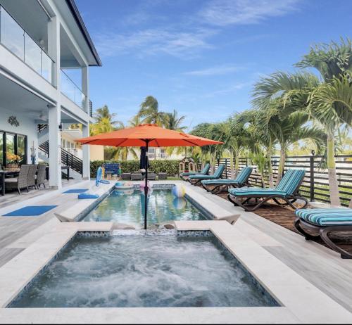 a swimming pool with an umbrella and chairs and a patio at Oceanfront 5BR+ Bonus Room•75’ Dock •Pool-Spa •Kids area •Walk to Sombrero Beach in Marathon