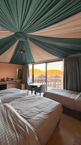 a bedroom with two beds and a table and a window at Wadi Rum Bella Rose Luxury Camp in Disah