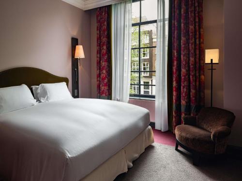 a bedroom with a bed and a window and a chair at Sofitel Legend The Grand Amsterdam in Amsterdam
