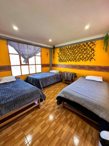 two beds in a room with yellow walls and wooden floors at Hospedaje Vista Ausangate in Labramarca