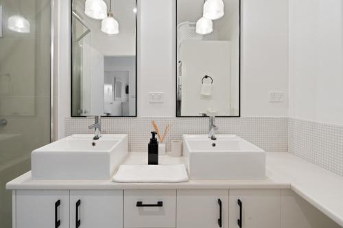 a white bathroom with two sinks and a mirror at Riverfront 2BR Apt with Views, Balcony & Parking in Maroochydore