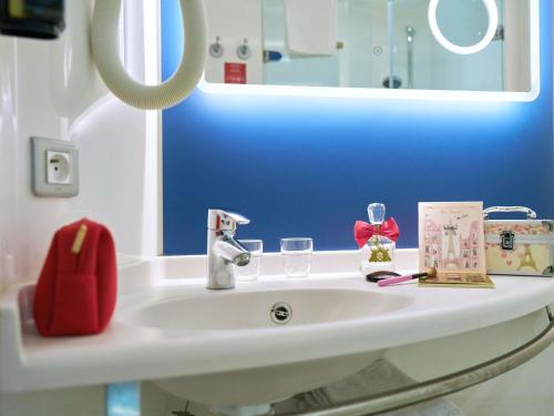a bathroom sink with a red purse and glasses on it at Ibis Sarlat Centre in Sarlat-la-Canéda