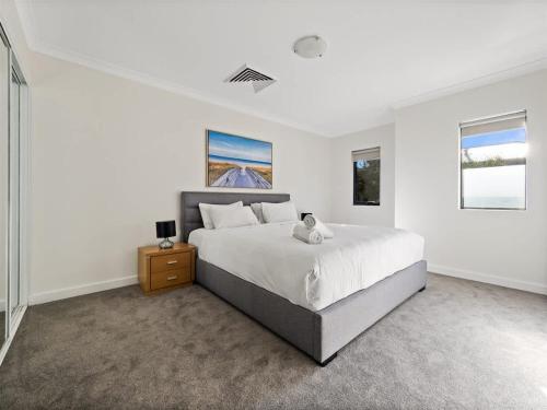 a white bedroom with a large bed and two windows at Surfside 1 - An Unforgettable Yallingup Experience in Yallingup