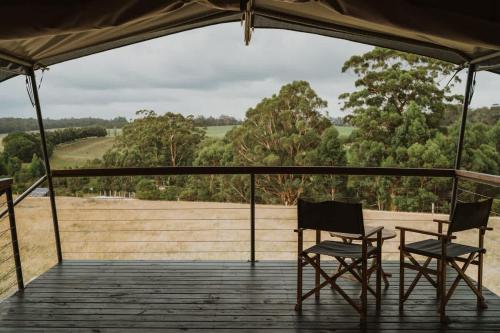two chairs and a table on a deck with trees at Wandagar Eco Tent - Carnaby in Pemberton