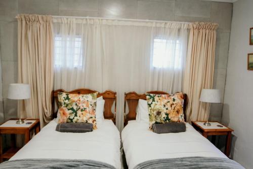 two beds in a bedroom with curtains and two lamps at Fynbos cottage in Bethlehem