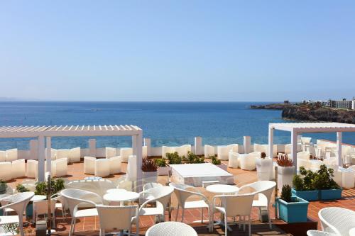 a patio with white tables and chairs and the ocean at Sandos Papagayo in Playa Blanca