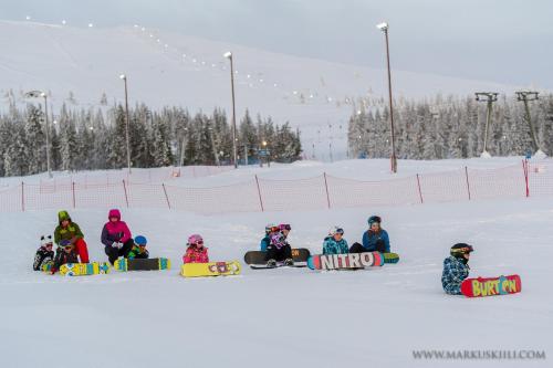 a group of people sitting in the snow with snowboards at Ylläksen Yöpuu in Äkäslompolo