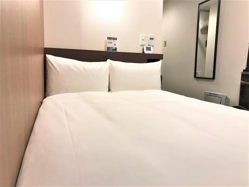 a large white bed with white sheets and pillows at Smile Hotel Mito in Mito
