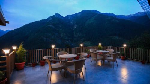 a balcony with tables and chairs and a view of mountains at Echor Mountain Crest Jibhi in Jibhi