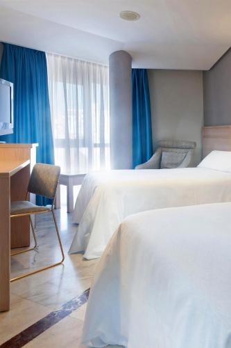a hotel room with two beds and a desk at Hotel Puertollano in Puertollano