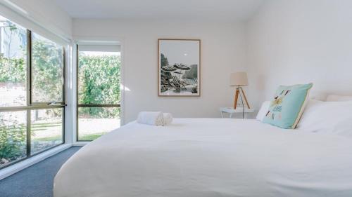 a white bedroom with a large white bed and windows at Blissful Escape in Portsea