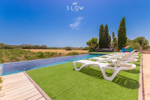 a row of white lounge chairs sitting next to a pool at Villa Son Bennasar by Slow Villas in Felanitx