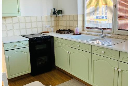 a kitchen with green cabinets and a black dishwasher at Cozy Grays Apartment in Grays Thurrock