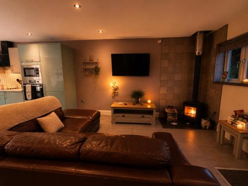 a living room with a brown leather couch and a television at Hawthorn Cottage in Tenby